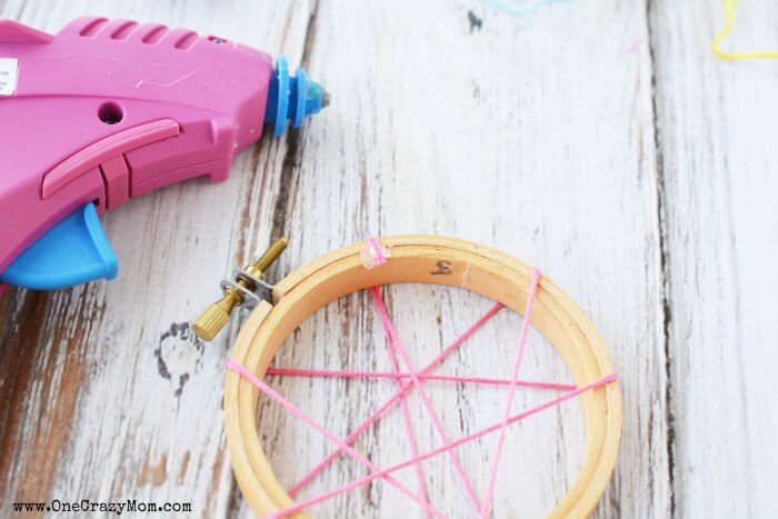 Wooden hoop with the embroidery floss wrapped around it with a hot glue gun on the side