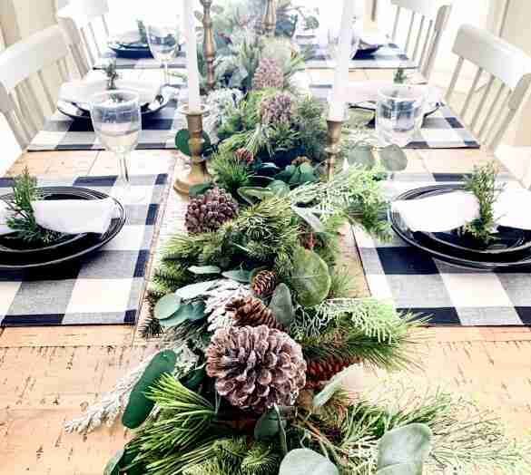 Black and white placemats and greenery table runner on table.