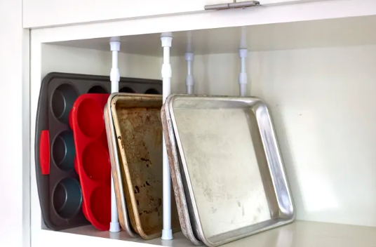 Tension rods under a cabinet organizing pans.