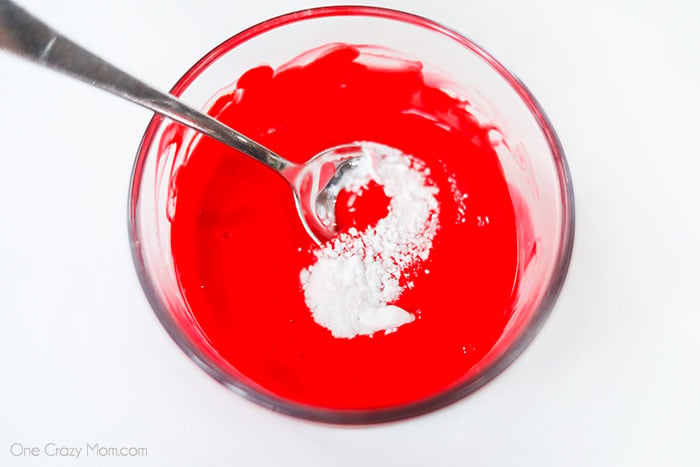 Red Glue in a bowl mixing with baking soda in a bowl with a spoon