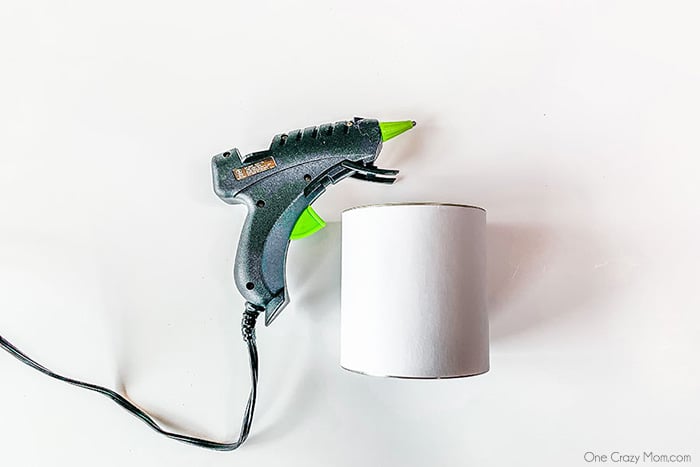 Glue gun attaching white paper to can.