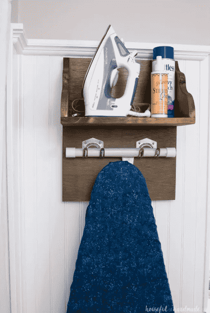 Iron holder mounted to wall with storage shelves for supplies.