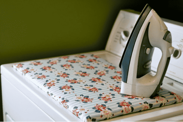 Ironing board on dryer with iron.