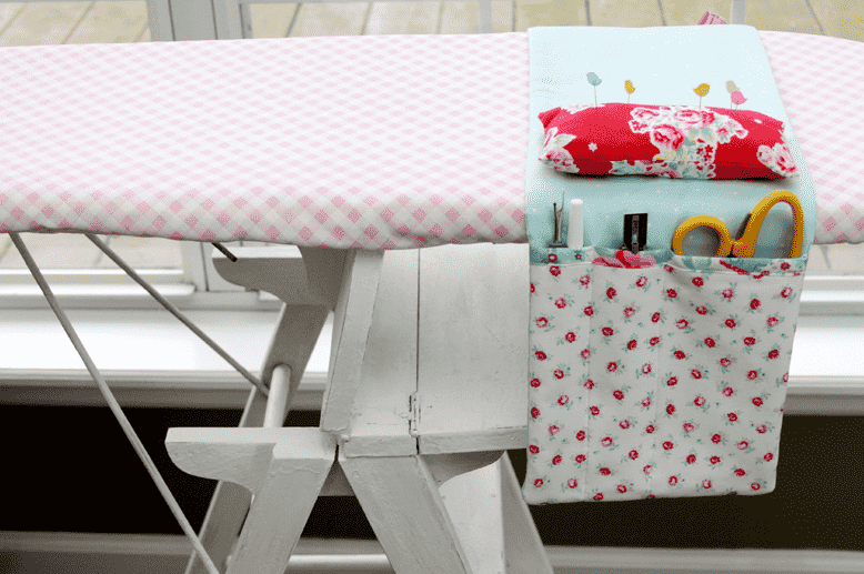 Ironing board organizer for supplies hanging over ironing board.