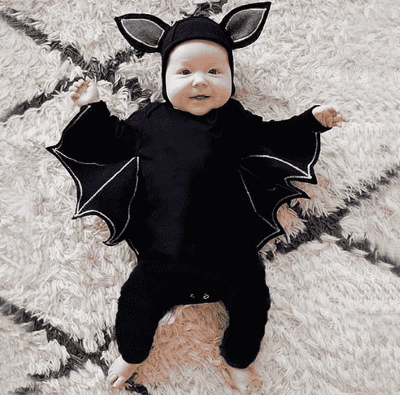 Baby in a bat costume laying on a rug.