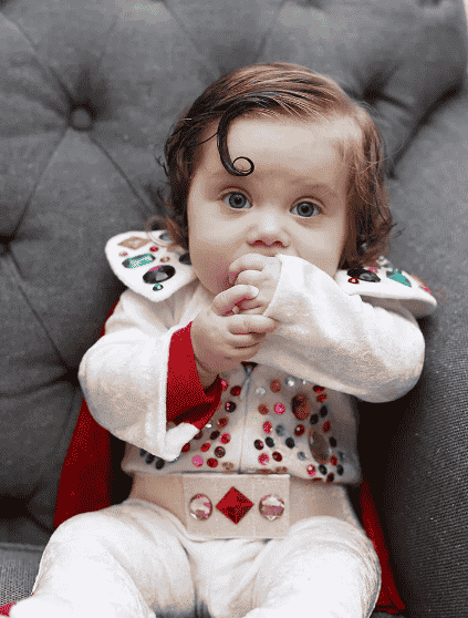 Baby in Elvis costume sitting on the couch.