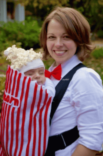 Mom holding baby dressed as popcorn in baby carrier.