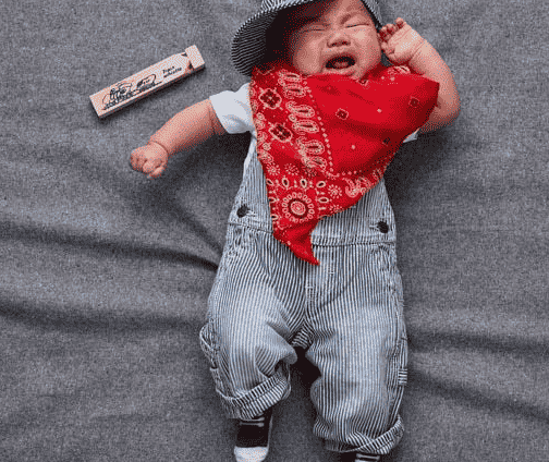 Baby in overalls dressed as train conductor.