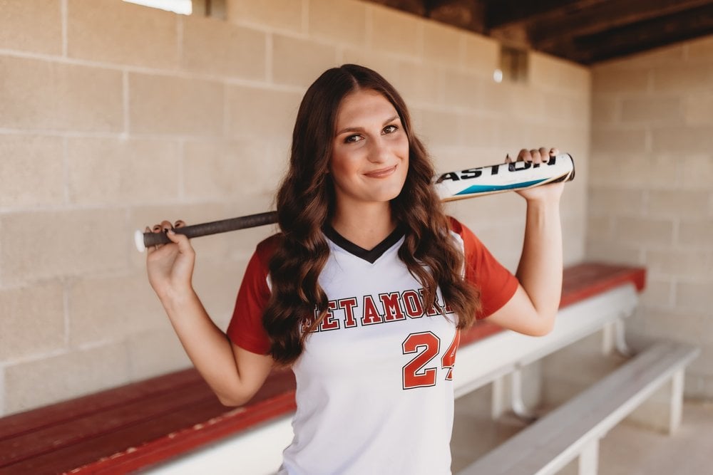 Girl with softball bat in dugout.