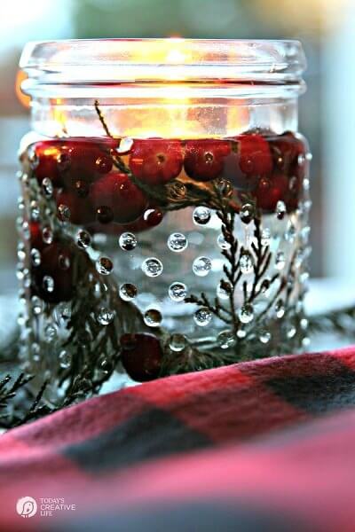 Create Christmas table top decorations with these easy ideas. 15 DIY Christmas table decorations anyone can make. Simple Christmas table decoration ideas. Decorative glass jar with greenery, berries, water and floating candle.