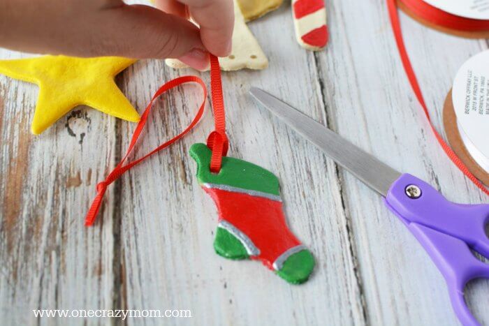 Make special memories with this simple and fun Salt Dough Ornament Recipe for Christmas. Learn how to make salt dough ornaments so easy the entire family can help! This great ornament DIY is perfect for kids. #onecrazymom #christmasornaments #DIYornaments #saltdoughornaments Red string going on ornaments.