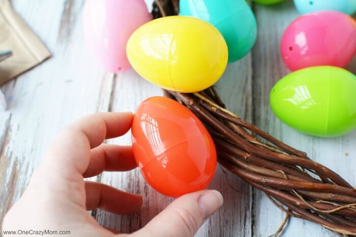 Make this DIY Easter Egg Wreath with items from the dollar store. You will love this easy Easter Egg Wreath DIY. Try this frugal Easter craft today. Egg being attached to wreath.