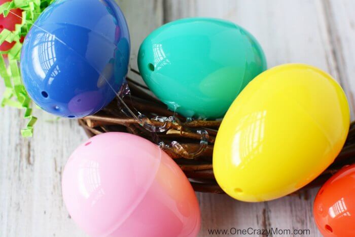 Make this DIY Easter Egg Wreath with items from the dollar store. You will love this easy Easter Egg Wreath DIY. Try this frugal Easter craft today. Egg being attached to wreath.