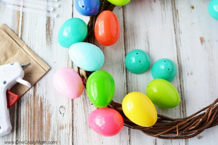 Make this DIY Easter Egg Wreath with items from the dollar store. You will love this easy Easter Egg Wreath DIY. Try this frugal Easter craft today. Eggs being attached to wreath.