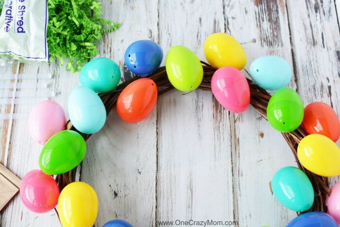 Make this DIY Easter Egg Wreath with items from the dollar store. You will love this easy Easter Egg Wreath DIY. Try this frugal Easter craft today. Eggs being attached to wreath.