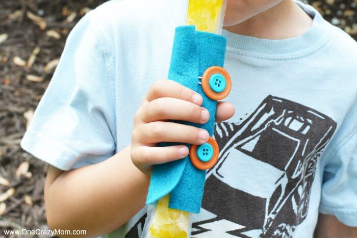 Learn how to make a DIY popsicle holder. It is so simple to make a homemade popsicle sleeve. Kid's will love having their very own popsicle holder. Little hands will not get cold using a homemade popsicle holder. They are so easy to make and budget friendly! Child holding popsicle in holder.