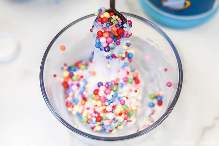 Learn how to make Birthday Cake Slime with only 3 ingredients. Adults and kids love making this birthday cake foam slime recipe in just minutes. It's easy to make this DIY slime recipe! #onecrazymom #slimerecipes #birthdaycakeslime Bowl with ingredients being mixed.