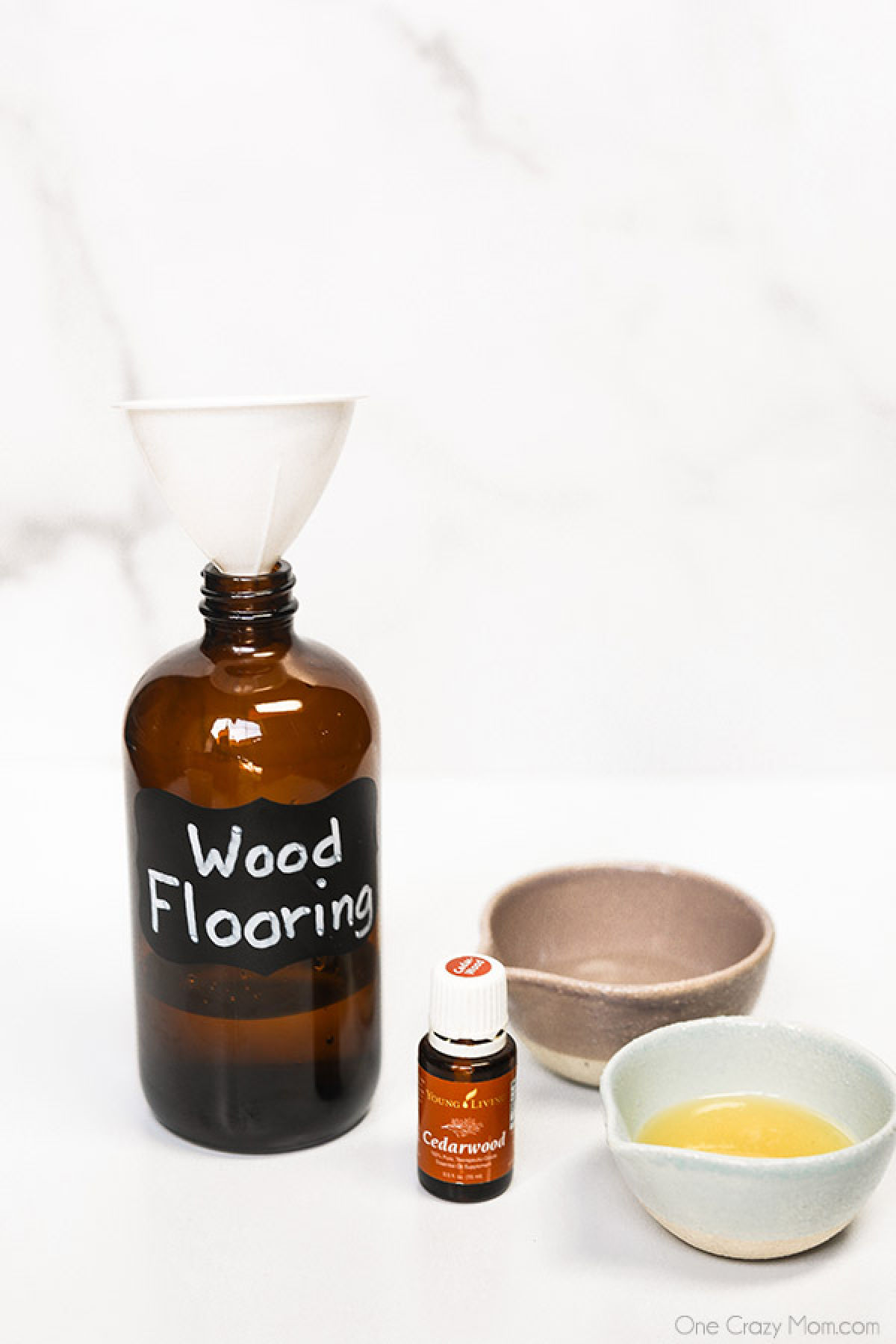 Make this DIY hardwood floor cleaner in just minutes for an all natural cleaner you will love. From floors to trim and more, your wood will be so clean. Glass Storage Bottle labeled with wood flooring with two bowls of vinegar and oil and a bottle of essential oil