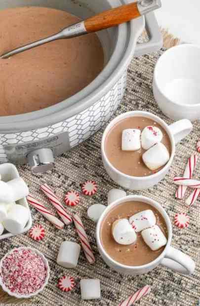 Crock Pot Hot Chocolate in the slow cooker surrounded by mugs.