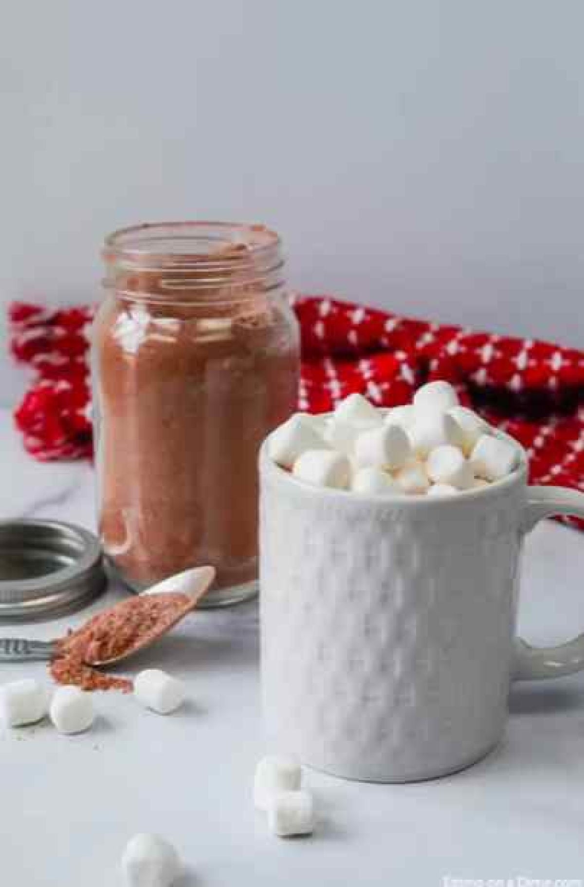 Jar of hot cocoa mix with a cup of hot chocolate in front of it.