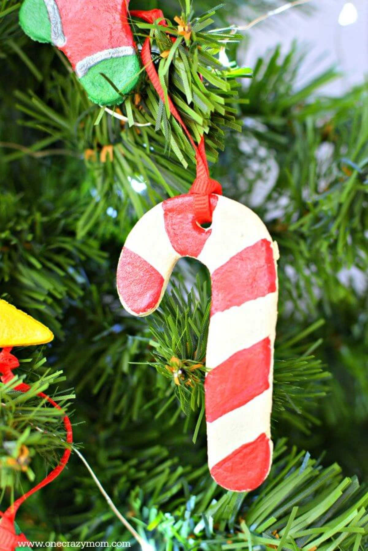 Make special memories with this simple and fun Salt Dough Ornament Recipe for Christmas. Learn how to make salt dough ornaments so easy the entire family can help! This great ornament DIY is perfect for kids. #onecrazymom #christmasornaments #DIYornaments #saltdoughornaments Candy Cane Salt dough ornament on a tree.