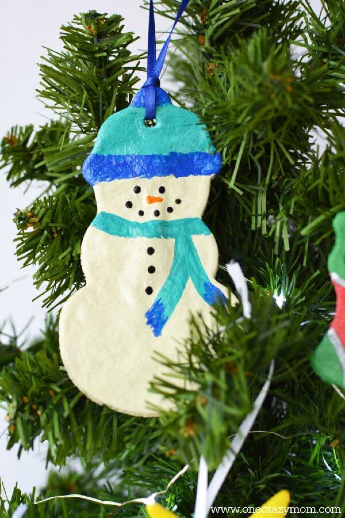 Make special memories with this simple and fun Salt Dough Ornament Recipe for Christmas. Learn how to make salt dough ornaments so easy the entire family can help! This great ornament DIY is perfect for kids. #onecrazymom #christmasornaments #DIYornaments #saltdoughornaments Snowman Salt dough ornament on a tree.