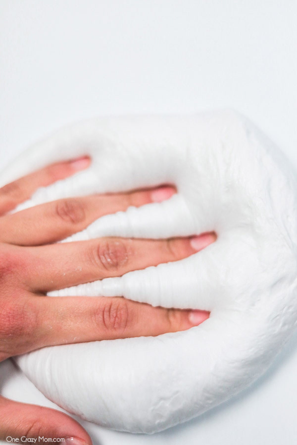 Snow Slime is so fun to make and only requires a few supplies. This is super easy and the kids will go crazy over this snow slime recipe. Snow slime in a pile with a hand on top.