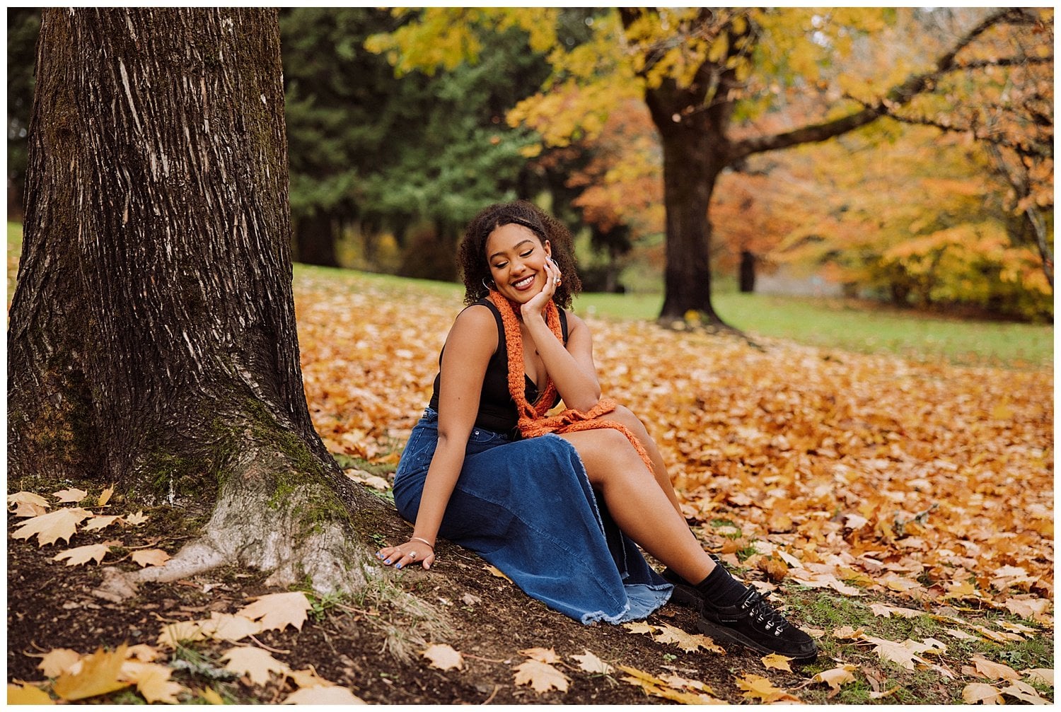 Girl sitting by tree with fall leaves.